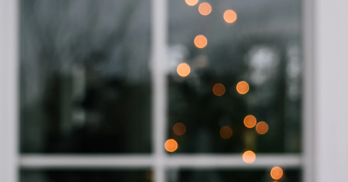 Persoon kijkt alleen uit het raam naar kerstverlichting op een winteravond