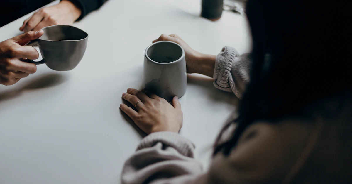 Twee volwassenen in een rustig gesprek aan tafel met een kop koffie